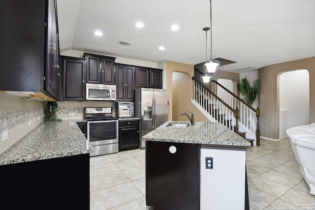 kitchen with sink, appliances with stainless steel finishes, backsplash, hanging light fixtures, and a kitchen island with sink