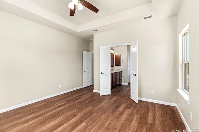 unfurnished bedroom featuring dark hardwood / wood-style floors, a raised ceiling, multiple windows, ceiling fan, and ensuite bathroom