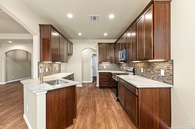 kitchen with stainless steel appliances, light hardwood / wood-style floors, decorative backsplash, sink, and light stone countertops