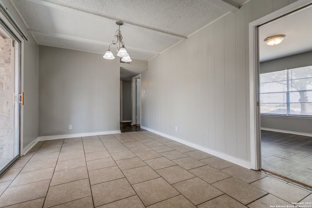 unfurnished room featuring wood walls, a chandelier, a textured ceiling, and light tile patterned floors