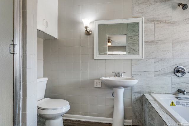 bathroom with tile walls, hardwood / wood-style floors, tiled bath, and toilet