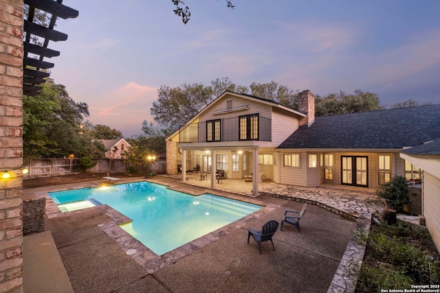 pool at dusk with a diving board, a patio, and a hot tub