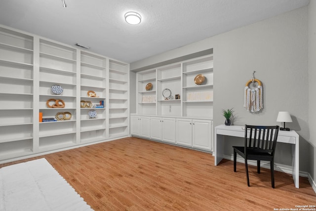 home office featuring light hardwood / wood-style floors, a textured ceiling, and built in desk