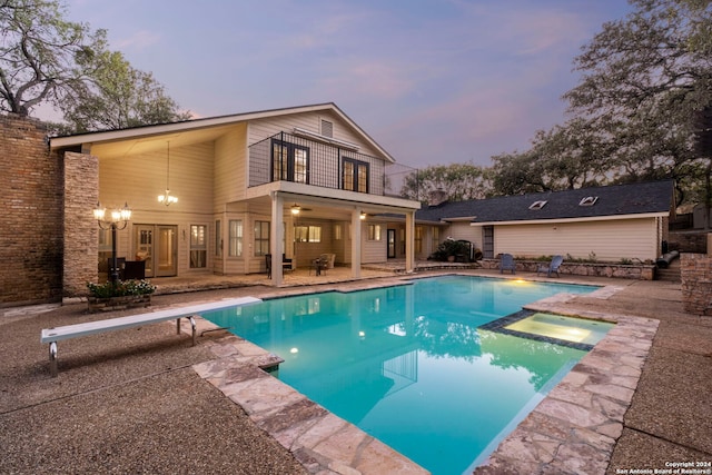 back house at dusk featuring a swimming pool with hot tub, a balcony, and a patio area