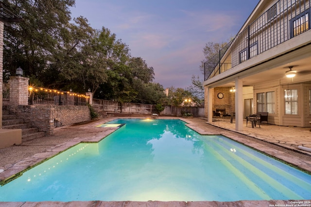 pool at dusk featuring ceiling fan and a patio area