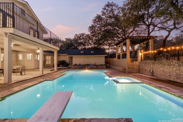 pool at dusk featuring a diving board, a patio, and an in ground hot tub