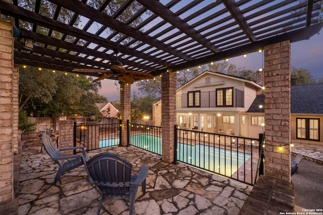 patio terrace at dusk with a pergola, an outbuilding, a fenced in pool, and ceiling fan