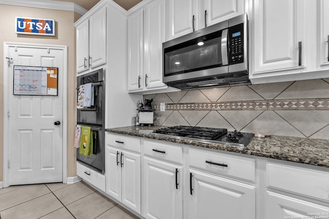 kitchen featuring white cabinets, light tile patterned floors, tasteful backsplash, appliances with stainless steel finishes, and dark stone countertops