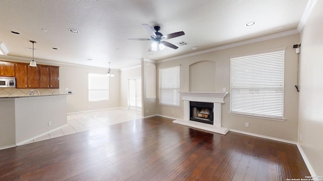 unfurnished living room featuring a wealth of natural light, hardwood / wood-style floors, ceiling fan, and crown molding