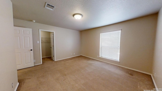 unfurnished bedroom featuring a textured ceiling, light carpet, a walk in closet, and a closet