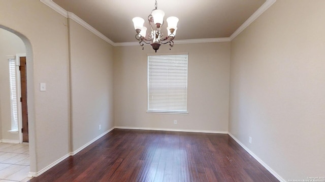 empty room with a wealth of natural light, hardwood / wood-style flooring, crown molding, and a notable chandelier