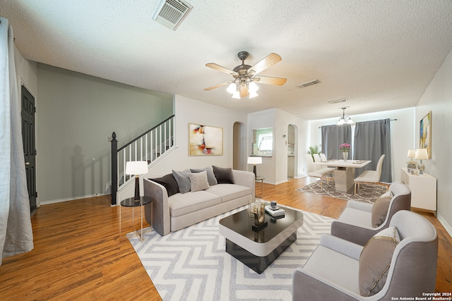 living room featuring ceiling fan with notable chandelier, a textured ceiling, and light wood-type flooring