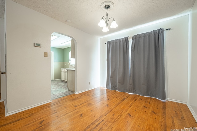 empty room featuring light hardwood / wood-style flooring, a textured ceiling, and a notable chandelier