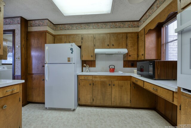 kitchen featuring washer / clothes dryer, a textured ceiling, white fridge, and stovetop