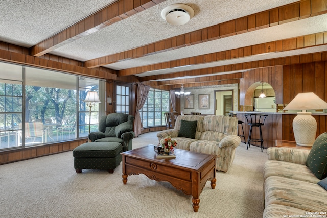 living room with carpet flooring, wooden walls, a textured ceiling, and beam ceiling