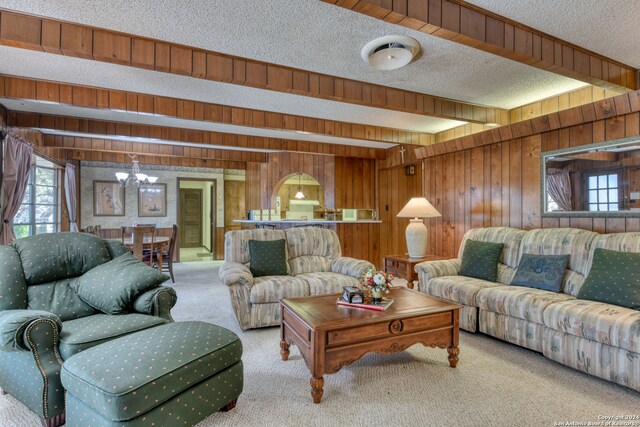 carpeted living room with a textured ceiling, wooden walls, beam ceiling, and an inviting chandelier