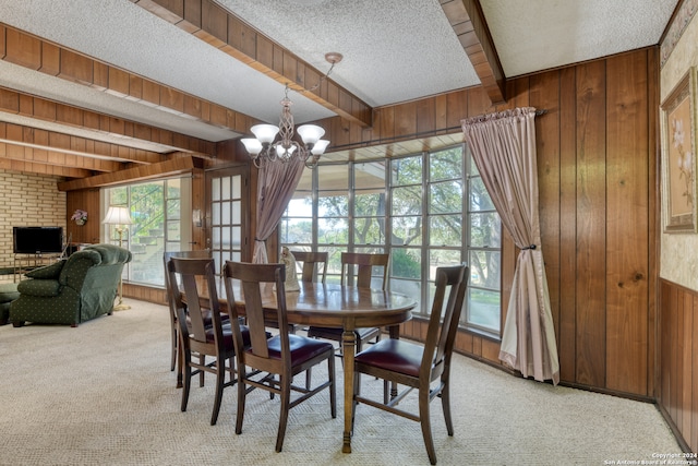 dining area with wooden walls, a textured ceiling, light colored carpet, and beam ceiling