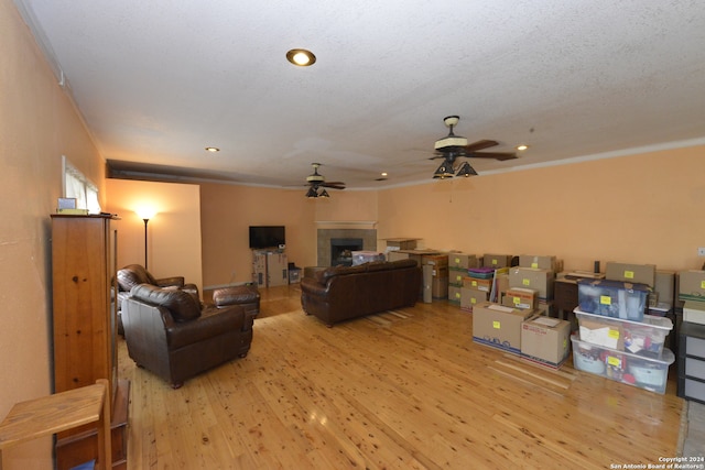 living room featuring crown molding, a textured ceiling, hardwood / wood-style floors, a tile fireplace, and ceiling fan