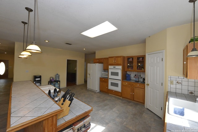 kitchen with sink, tasteful backsplash, white appliances, tile counters, and pendant lighting