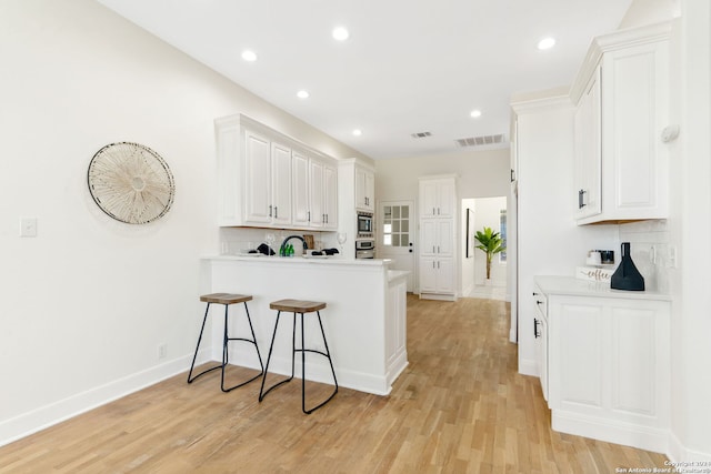 kitchen featuring kitchen peninsula, a kitchen bar, tasteful backsplash, light hardwood / wood-style flooring, and white cabinetry