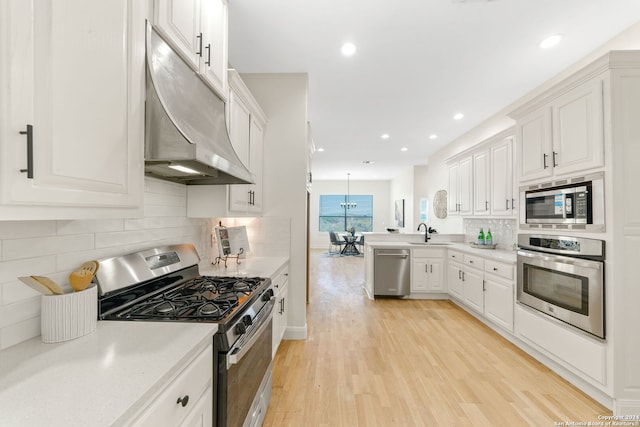 kitchen featuring white cabinets, sink, hanging light fixtures, light wood-type flooring, and stainless steel appliances