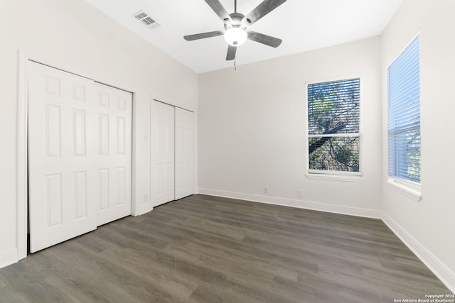 unfurnished bedroom featuring two closets, ceiling fan, and dark hardwood / wood-style floors