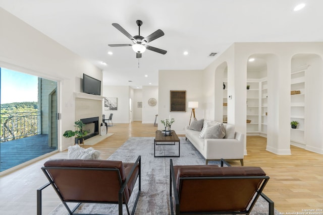 living room with ceiling fan, built in features, and light hardwood / wood-style flooring