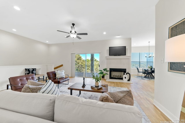 living room featuring ceiling fan with notable chandelier and light hardwood / wood-style flooring