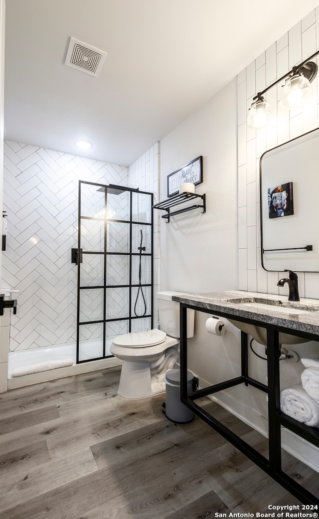 bathroom featuring sink, hardwood / wood-style flooring, toilet, and tiled shower