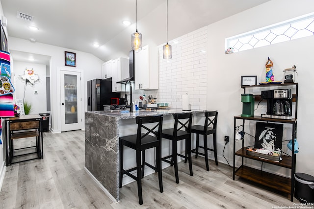 kitchen featuring kitchen peninsula, hanging light fixtures, a breakfast bar, stone countertops, and white cabinetry