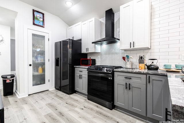 kitchen featuring light hardwood / wood-style floors, light stone counters, white cabinets, black appliances, and wall chimney range hood