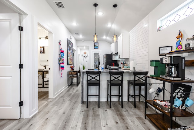 kitchen with white cabinetry, decorative light fixtures, a breakfast bar, kitchen peninsula, and light hardwood / wood-style flooring