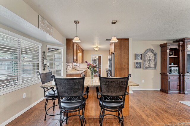 kitchen featuring stainless steel refrigerator, light stone counters, kitchen peninsula, pendant lighting, and dark hardwood / wood-style flooring