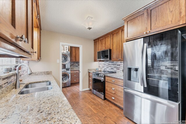 kitchen featuring stacked washer and clothes dryer, light stone counters, appliances with stainless steel finishes, sink, and light hardwood / wood-style flooring