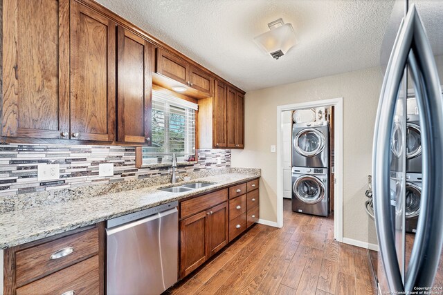 kitchen featuring stacked washer and clothes dryer, light stone counters, dark hardwood / wood-style flooring, sink, and dishwasher