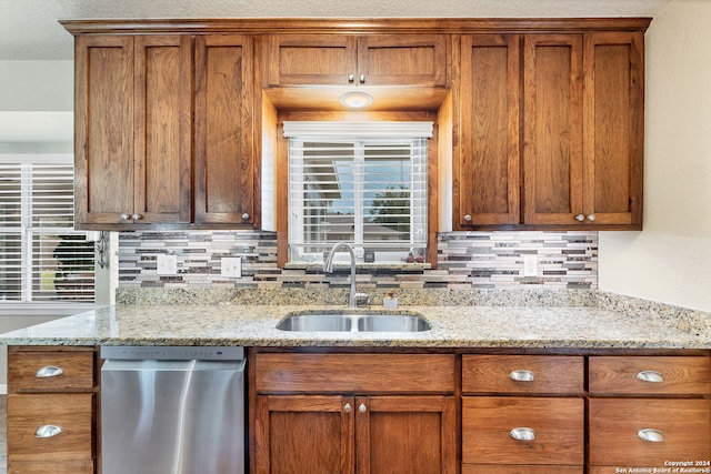 kitchen with stainless steel dishwasher, sink, and light stone countertops