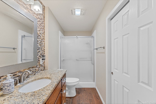 bathroom with a shower with door, backsplash, vanity, hardwood / wood-style floors, and toilet