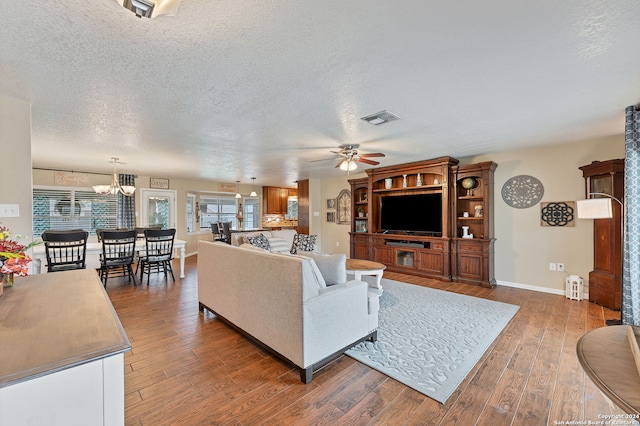 living room featuring ceiling fan with notable chandelier, dark wood-type flooring, and a textured ceiling