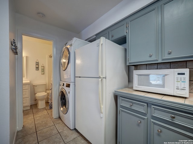 kitchen with light tile patterned floors, backsplash, tile counters, white appliances, and stacked washer and dryer