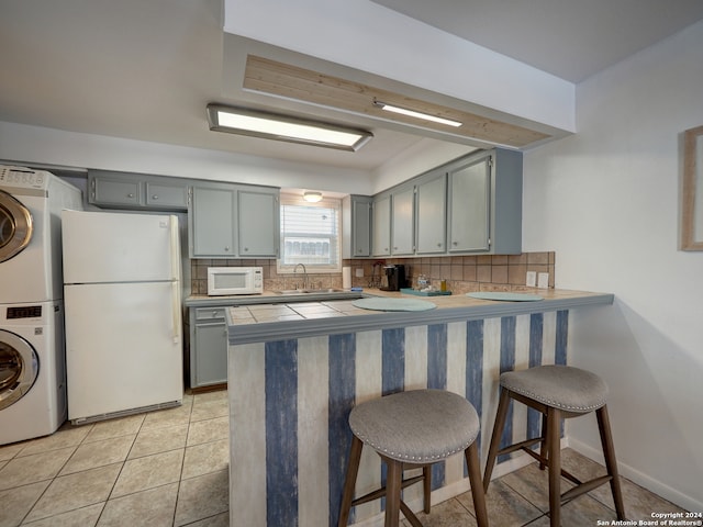 kitchen with white appliances, a breakfast bar area, stacked washer / dryer, and kitchen peninsula