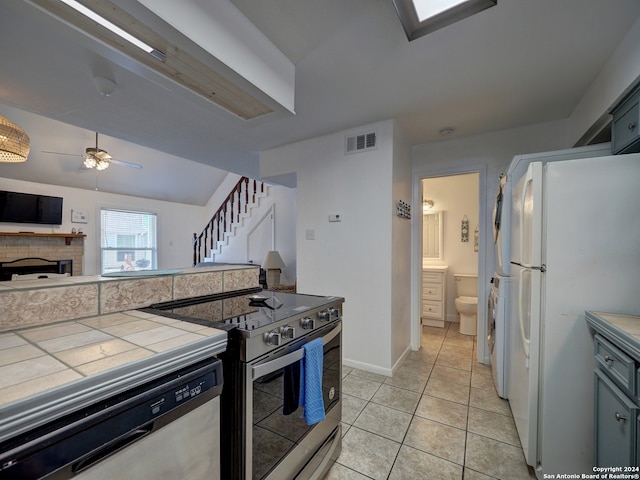 kitchen featuring light tile patterned flooring, stainless steel appliances, tile countertops, lofted ceiling, and ceiling fan