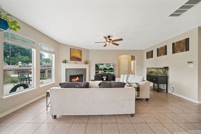 living room with ceiling fan, a tile fireplace, and light tile patterned floors