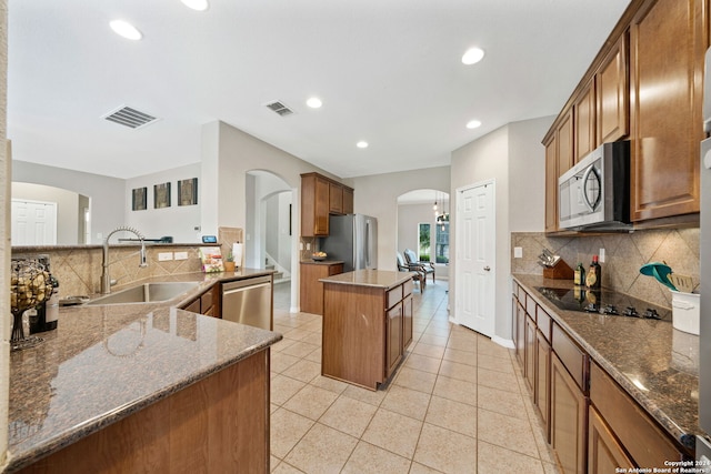 kitchen with stainless steel appliances, dark stone counters, sink, and a kitchen island