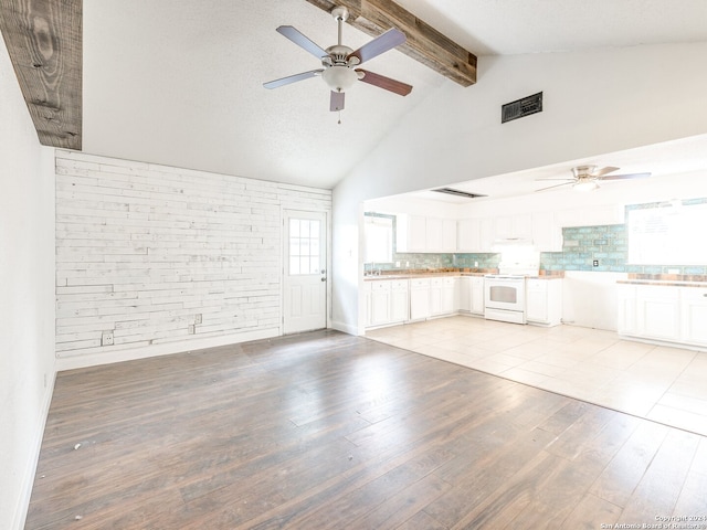 unfurnished living room with high vaulted ceiling, ceiling fan, light wood-type flooring, beam ceiling, and brick wall