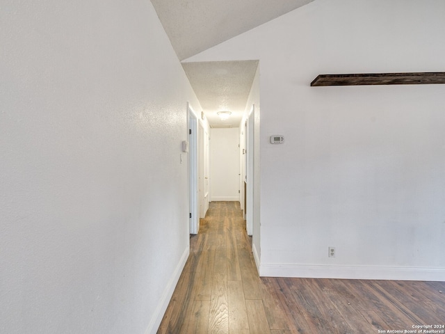 hallway with a textured ceiling, dark hardwood / wood-style flooring, and lofted ceiling