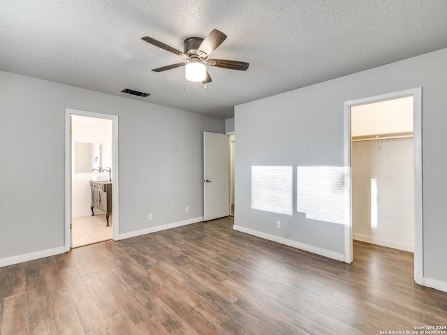 unfurnished bedroom with ensuite bathroom, a walk in closet, dark hardwood / wood-style floors, ceiling fan, and a textured ceiling