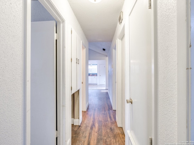 corridor featuring a textured ceiling, vaulted ceiling, and dark wood-type flooring