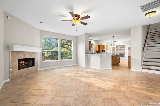 unfurnished living room with a tiled fireplace, ceiling fan, and light tile patterned flooring