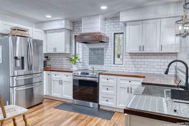 360 Benson Rd, Uvalde, TX 78801 - kitchen with stainless steel appliances, butcher block counters, custom exhaust hood, white cabinets, and a textured ceiling