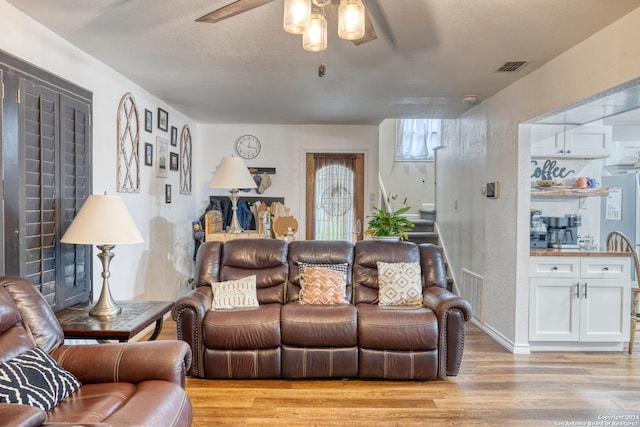 living room featuring a textured ceiling, light wood-type flooring, and ceiling fan